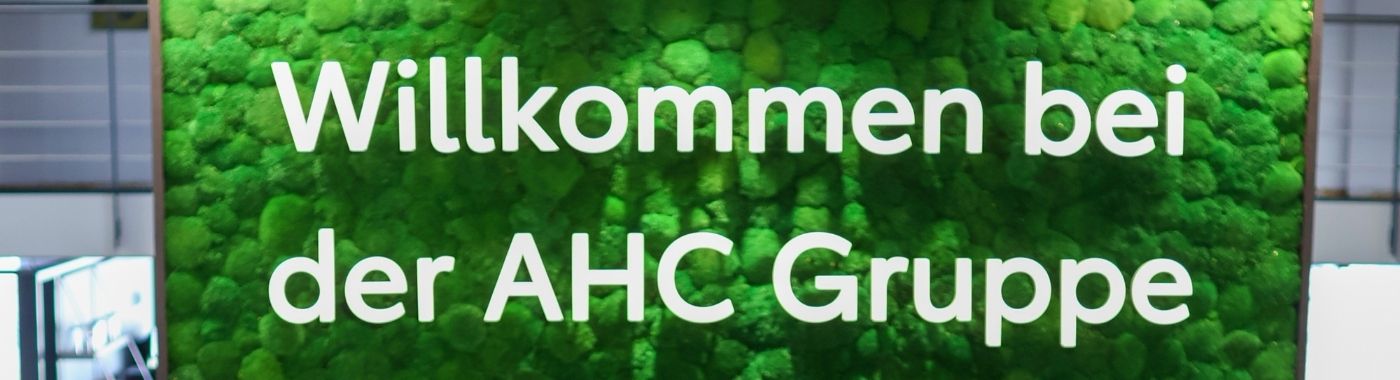 Grüne Mooswand mit dem Schriftzug Willkommen bei der AHC Gruppe