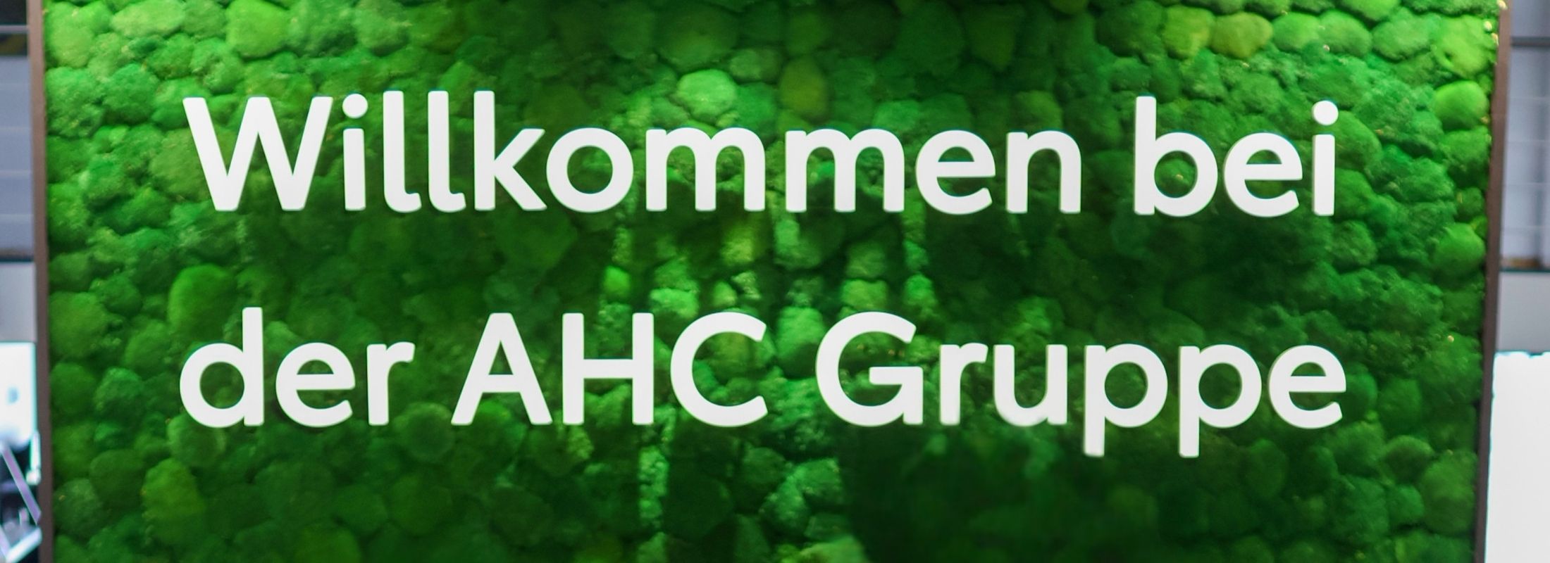 Grüne Mooswand mit dem Schriftzug Willkommen bei der AHC Gruppe