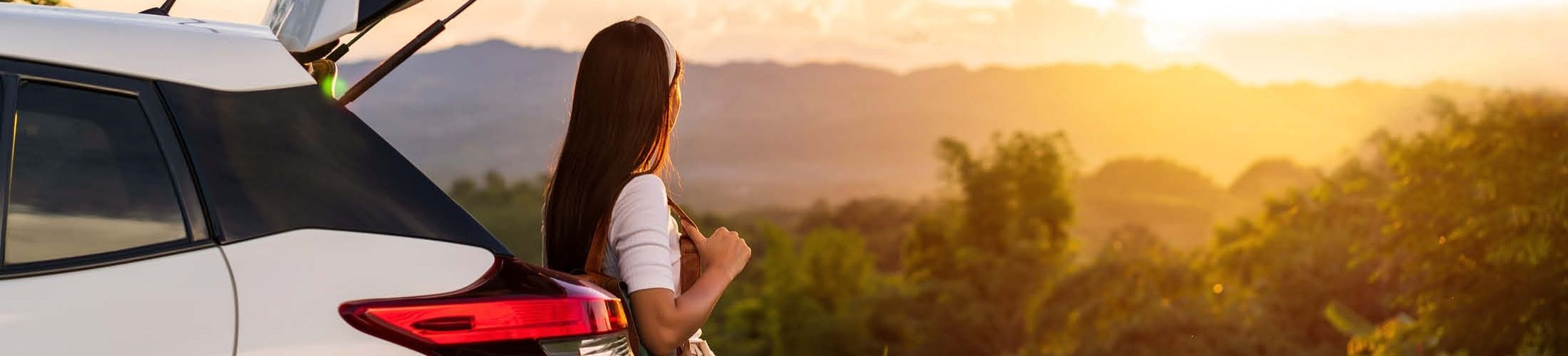 Frau sitzt in Kofferraum und schaut in die Ferne
